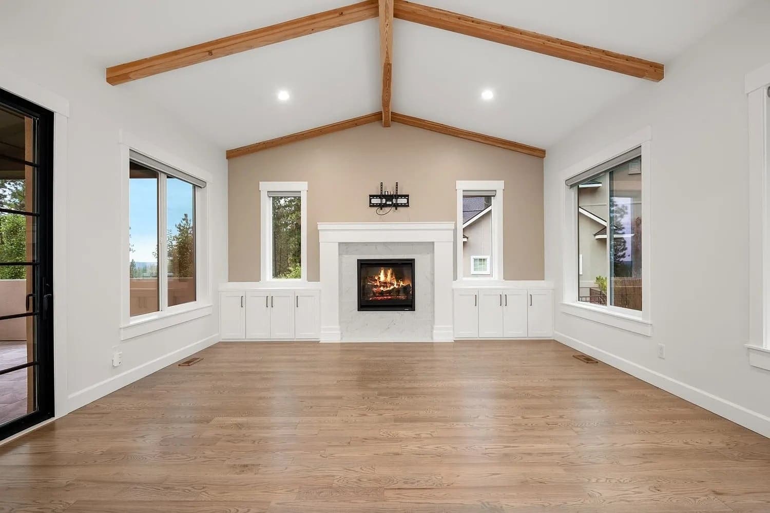 Spacious living room with vaulted ceiling, wooden beams, fireplace, and large windows.