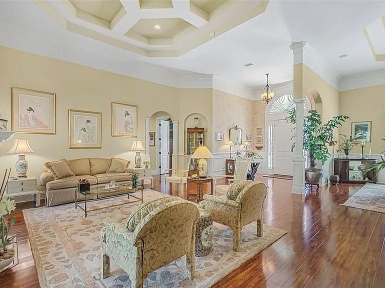 Spacious living room with elegant furniture, hardwood floors, and decorative ceiling. Large windows provide natural light.