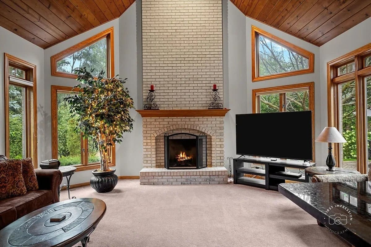 Spacious living room with large windows, brick fireplace, TV, and comfortable seating.