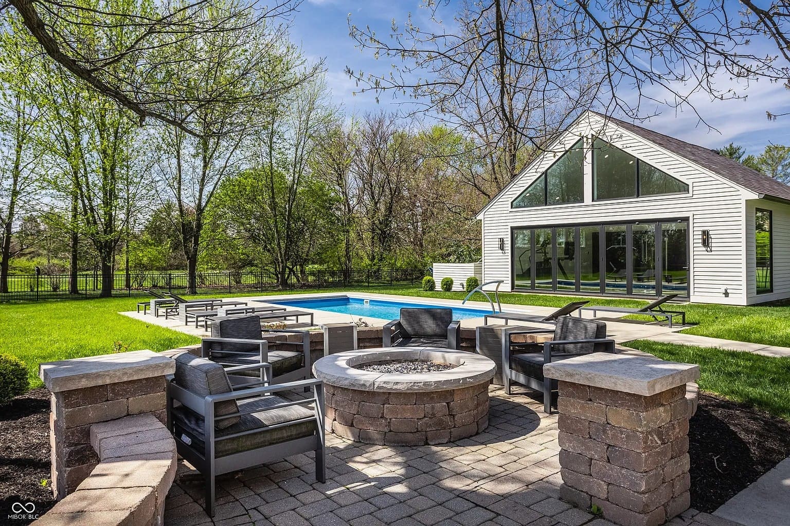 Backyard with a modern house, pool, fire pit, and patio seating surrounded by trees.