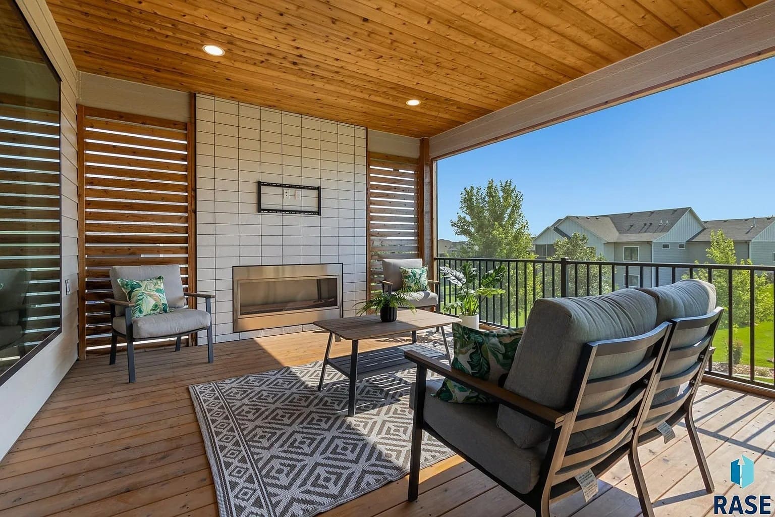 Covered patio with outdoor seating, fireplace, and view of suburban neighborhood.