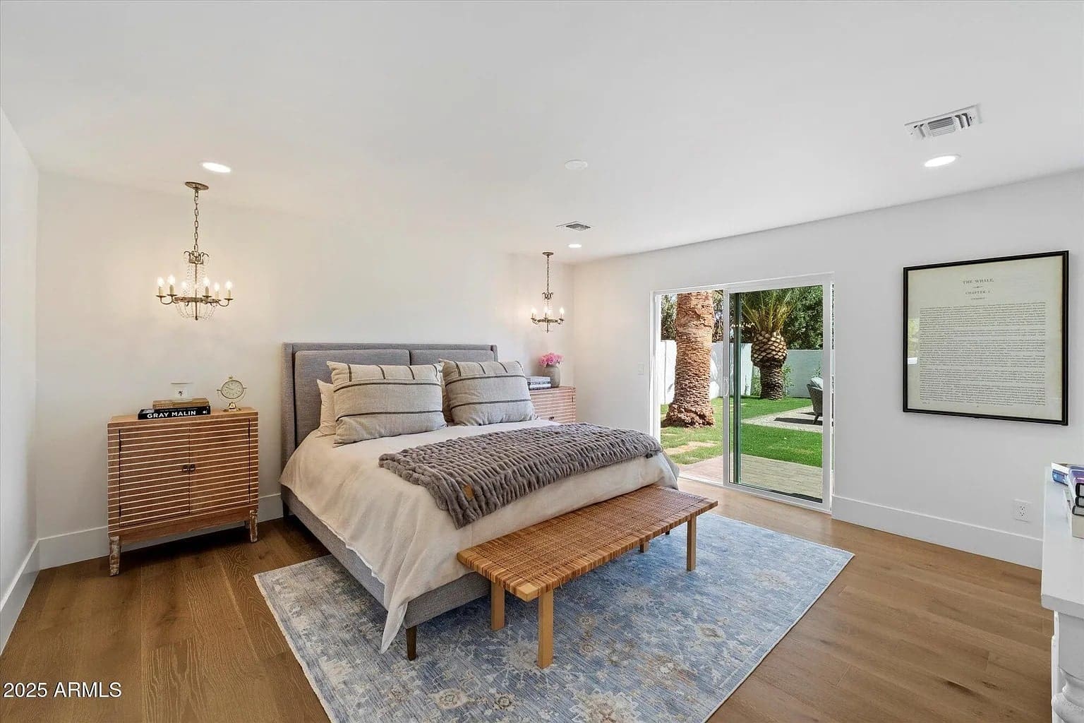 Modern bedroom with a large bed, wooden bench, chandelier, and sliding door to a garden.