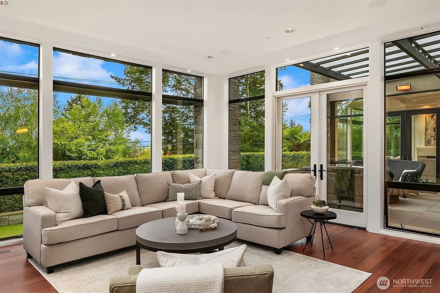 Modern living room with large windows, beige sectional sofa, round coffee table, and outdoor view.