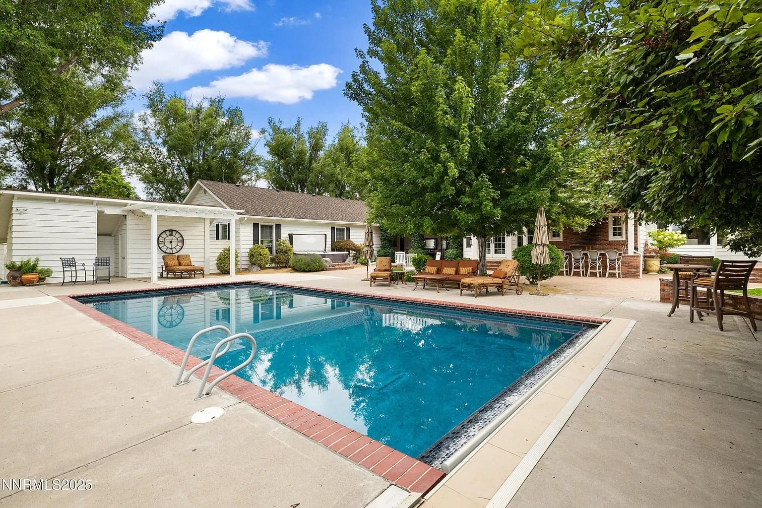 Backyard with a swimming pool, surrounded by trees, patio furniture, and a house.