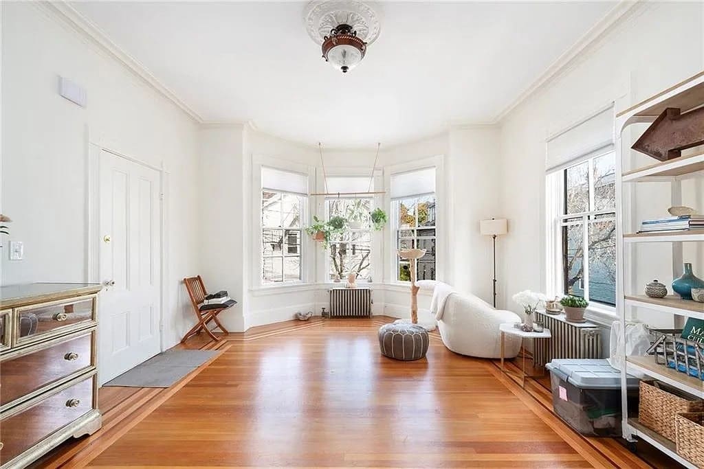 Bright, minimalist living room with hardwood floors, large windows, white walls, and simple furniture.
