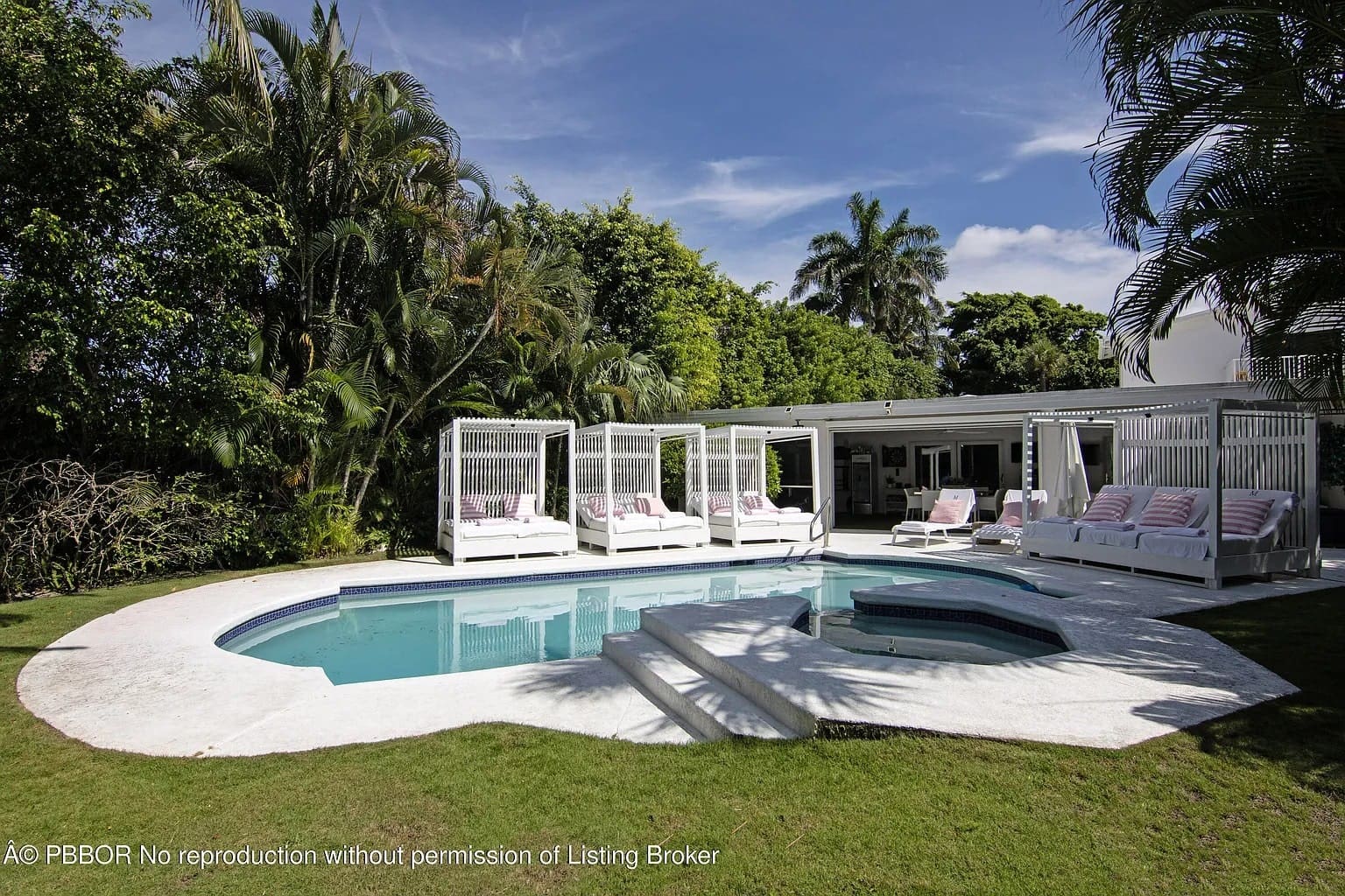 Outdoor pool area with white lounge beds, surrounded by lush greenery and a clear blue sky.