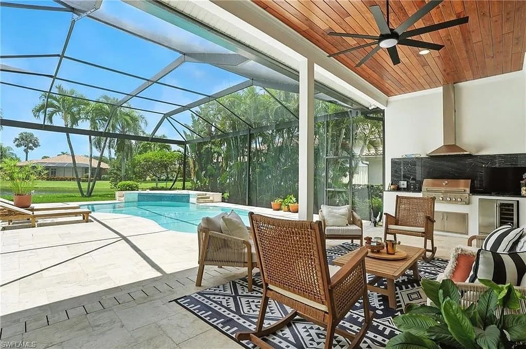 Covered patio with wicker furniture, ceiling fan, outdoor kitchen, and view of pool and garden.