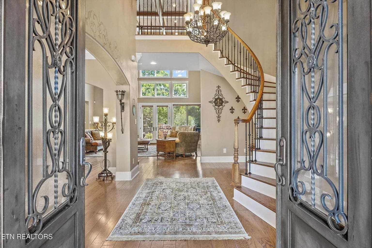 Elegant foyer with ornate double doors, spiral staircase, chandelier, and bright living area.