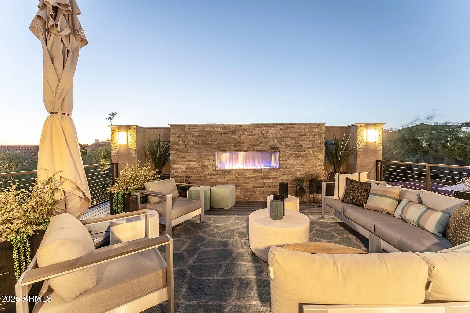 Rooftop patio with modern seating, a stone fireplace, and ambient lighting at dusk.