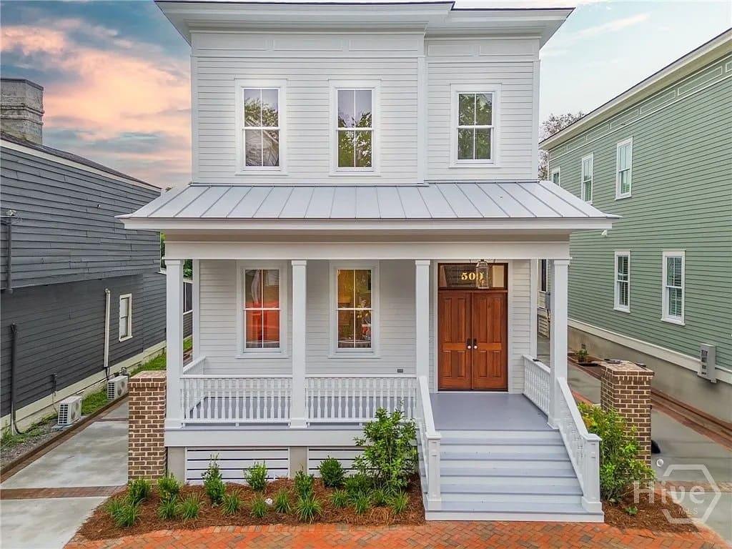 Two-story white house with a porch, wooden door, and brick pathway at sunset.