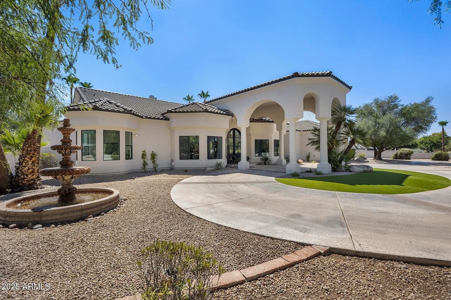 Elegant white stucco house with arched entry, circular driveway, and a fountain in the front yard.
