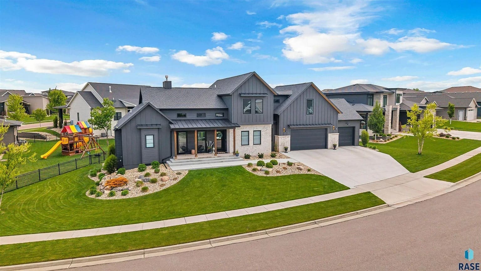 Modern suburban house with dark exterior, large windows, and a well-maintained lawn on a sunny day.