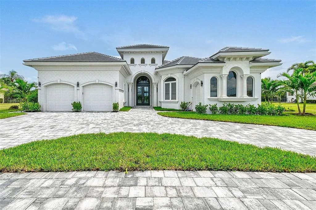 Modern white house with arched windows, two garages, and a paved driveway, surrounded by grass.

