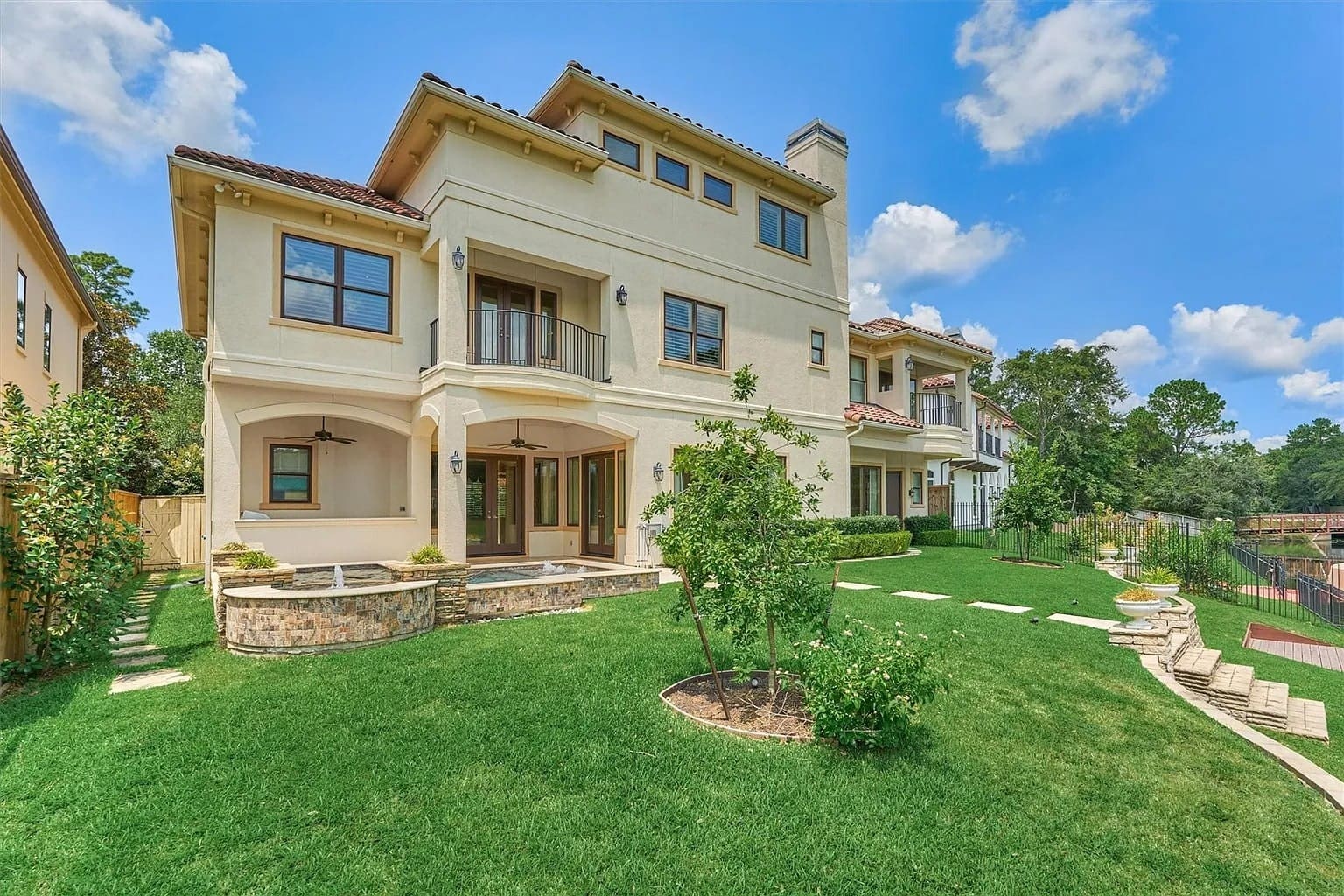 Large beige house with a balcony, manicured lawn, and clear blue sky.
