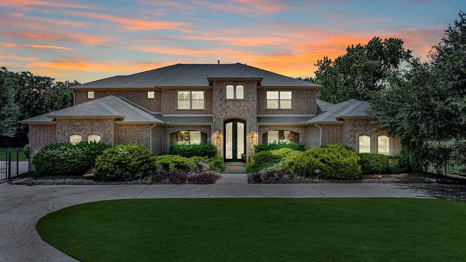 Large brick house with manicured lawn and sunset sky in the background.
