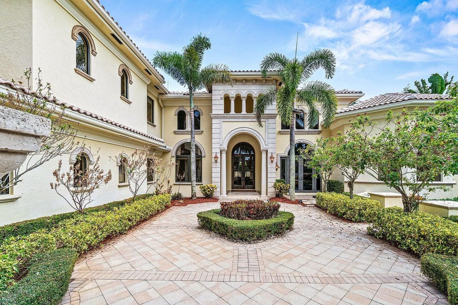 Large Mediterranean-style house with arched entrance, palm trees, and landscaped front yard.
