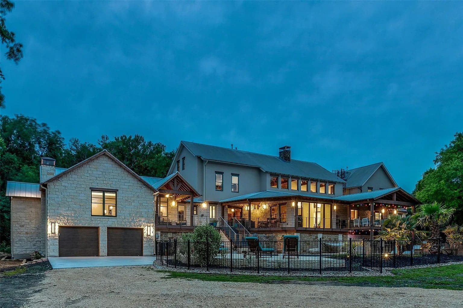Large modern house with stone and wood accents, illuminated at dusk, surrounded by trees.
