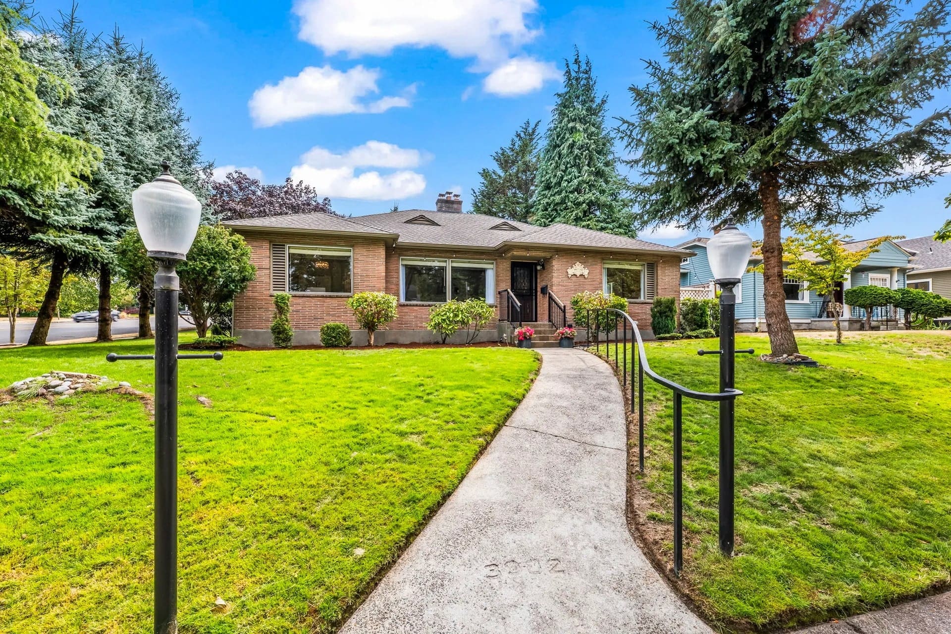 Brick house with large windows, surrounded by trees and a well-maintained lawn with a walkway.
