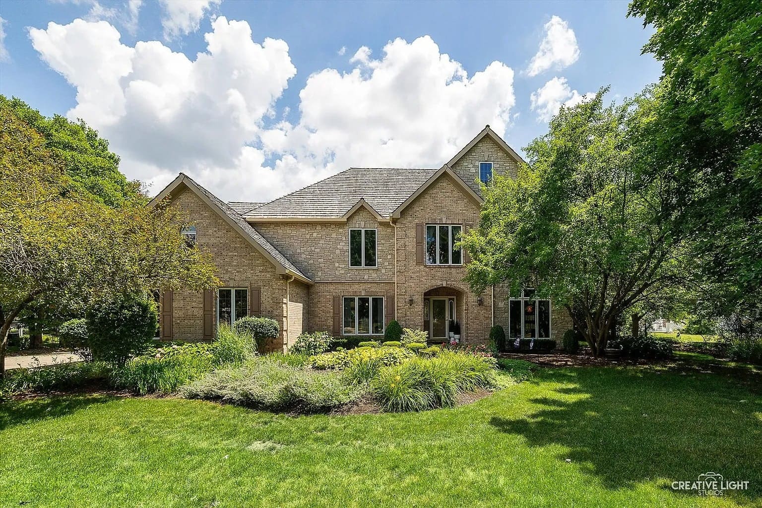 Large brick house with gabled roof, surrounded by trees and a well-maintained lawn.
