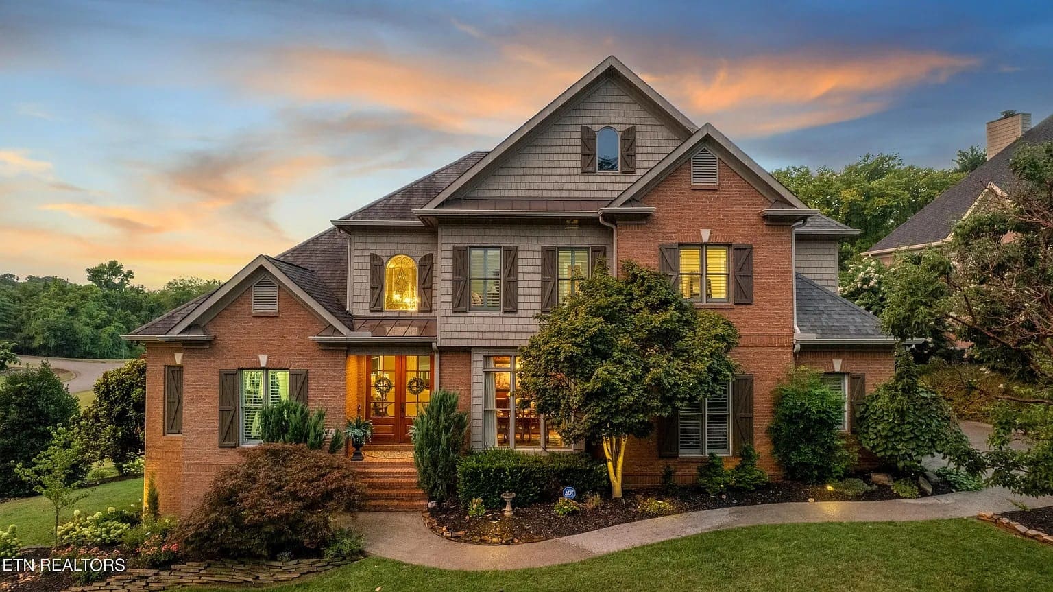 Two-story brick house with landscaped front yard, illuminated at dusk under a colorful sky.