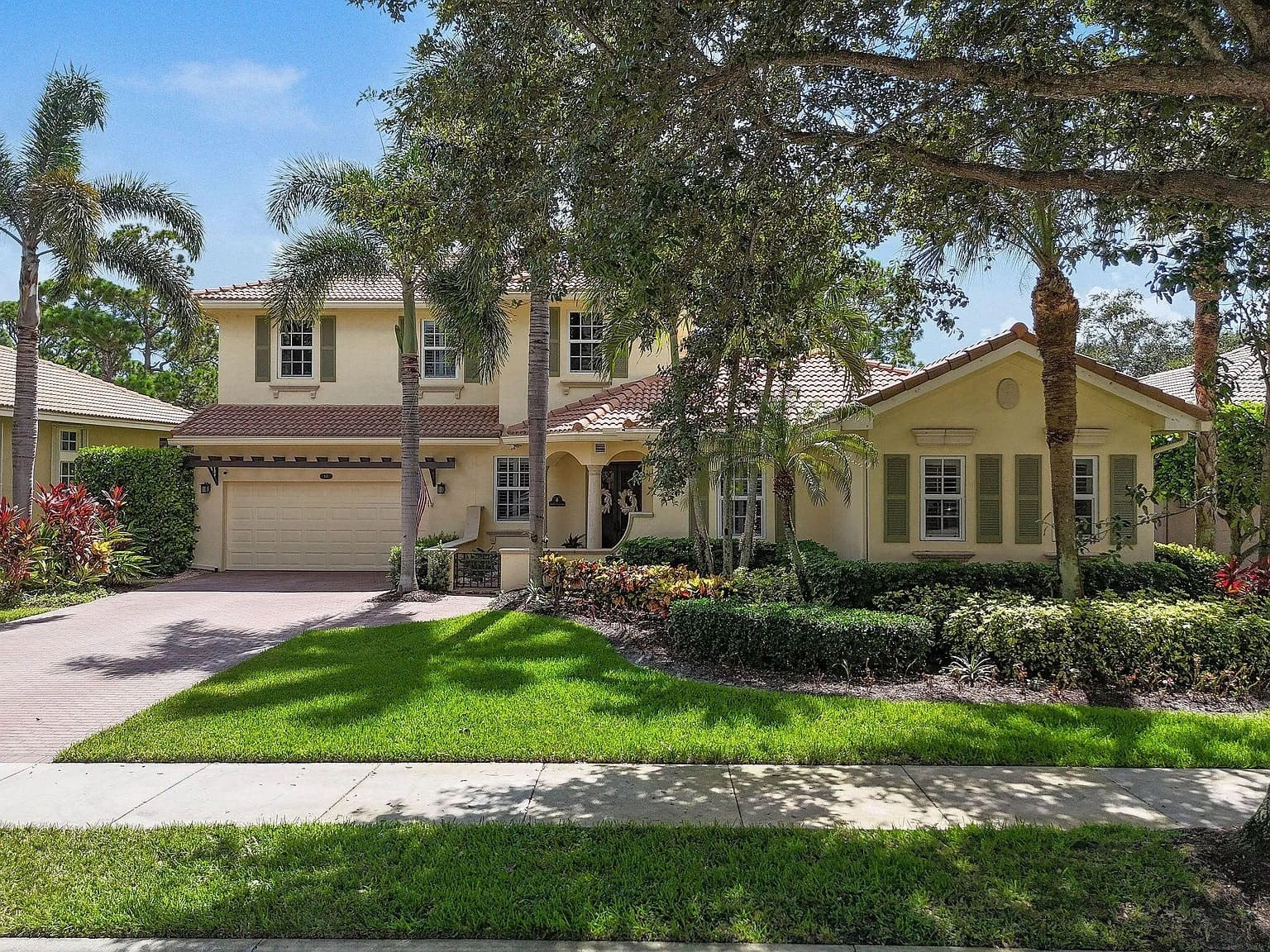Two-story yellow house with a tiled roof, surrounded by palm trees and a well-maintained lawn.

