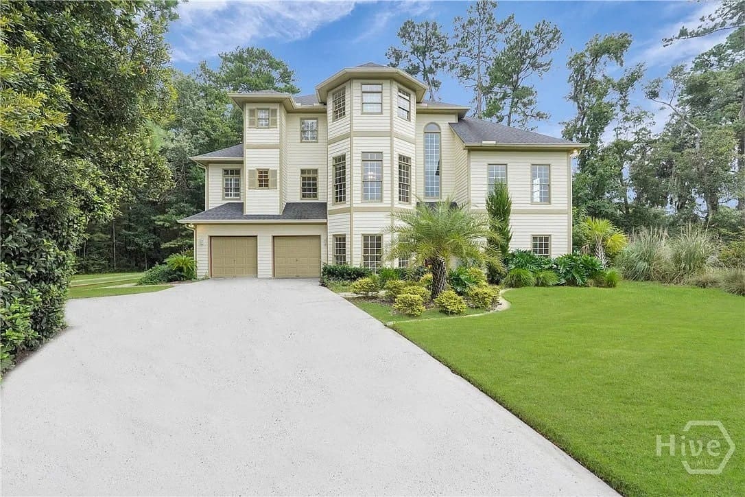 Large three-story house with a two-car garage, surrounded by trees and a manicured lawn.
