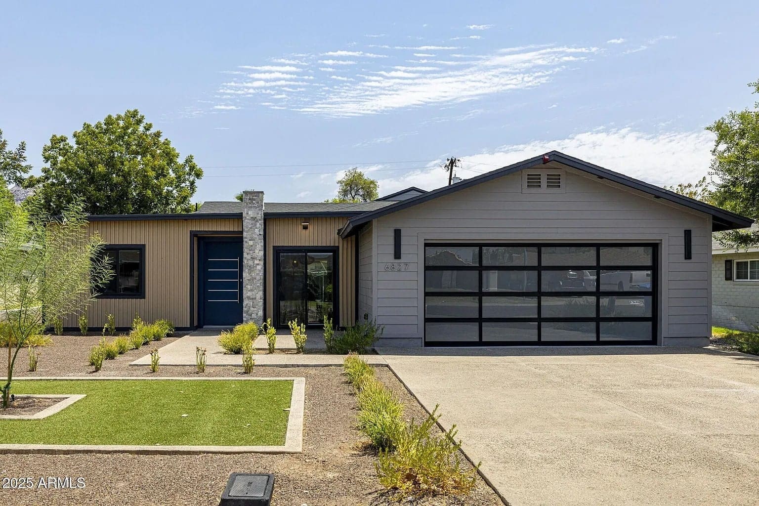 Modern single-story house with large glass garage door and landscaped front yard.
