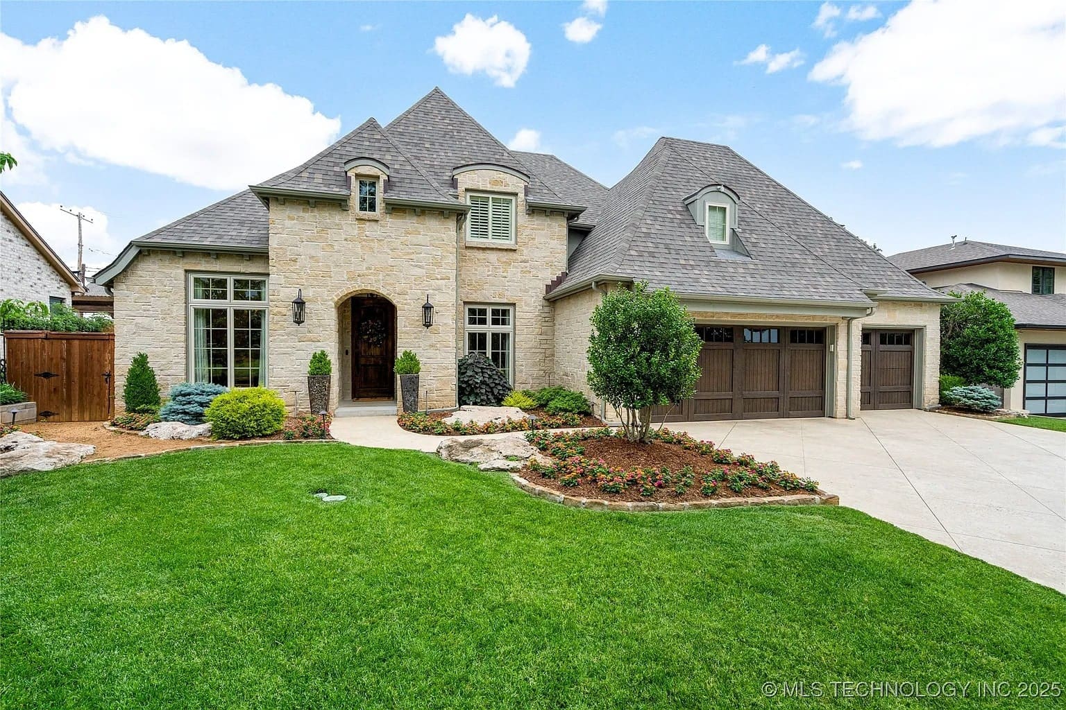 Stone house with steep roof, manicured lawn, and a two-car garage on a sunny day.
