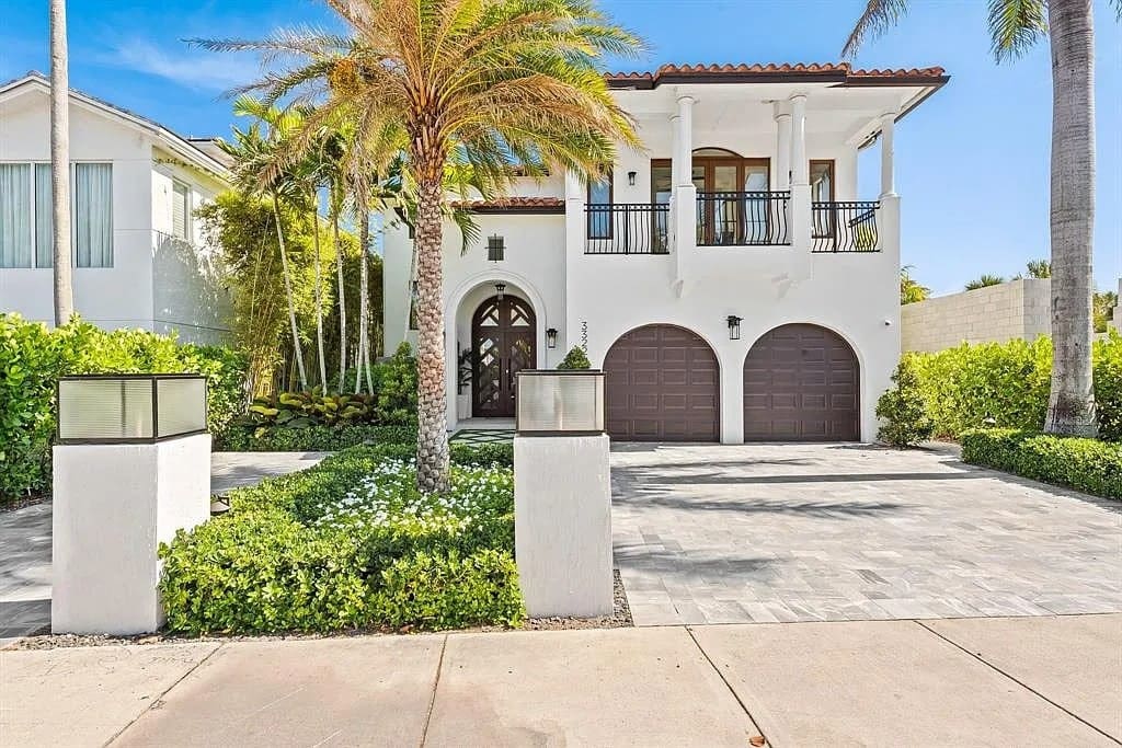 Two-story Mediterranean-style house with palm trees, arched entrance, and a double garage.

