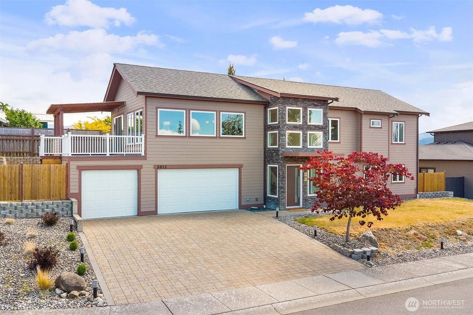 Two-story modern house with large windows, three-car garage, and a small front yard tree.
