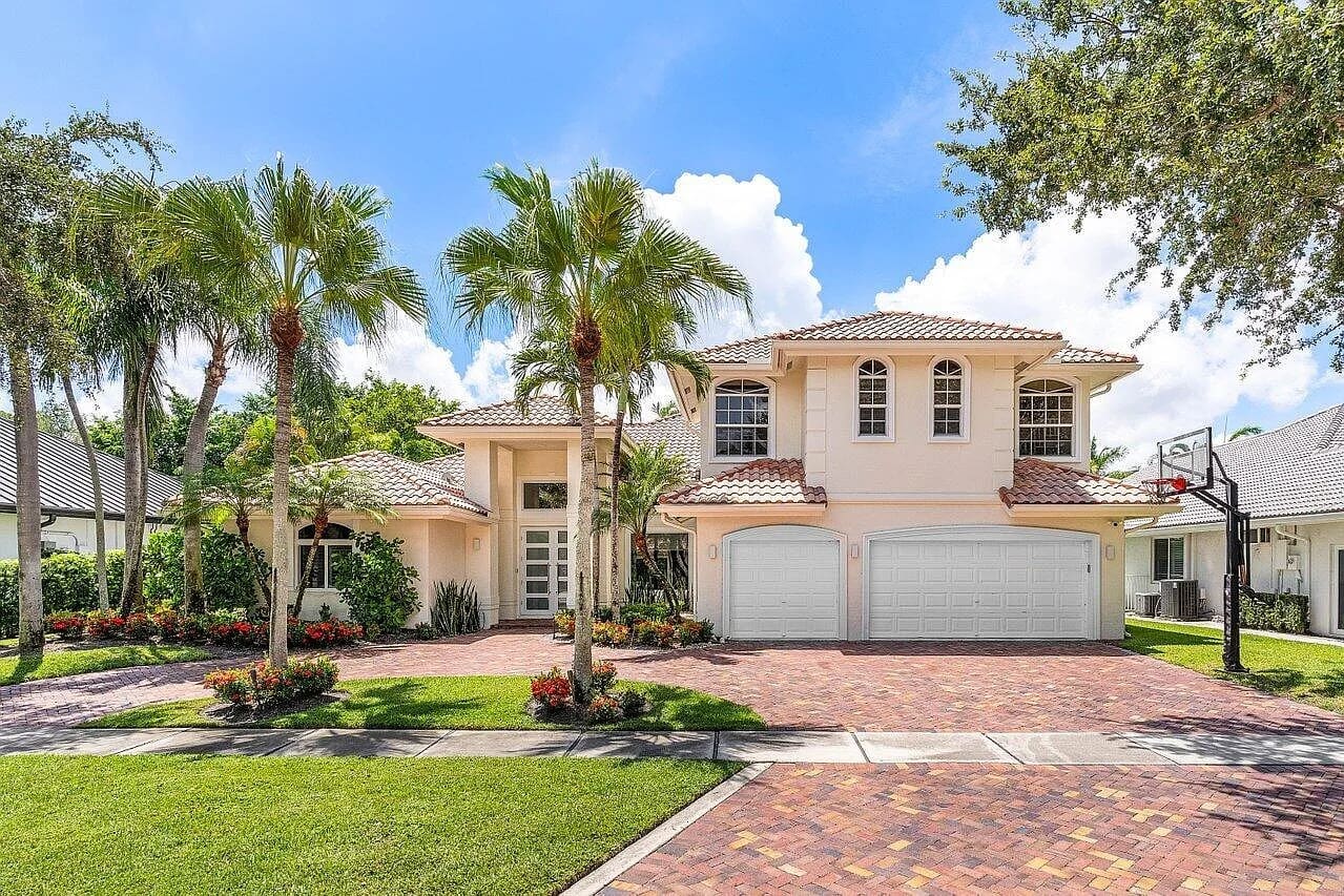 A large, two-story house with palm trees, a brick driveway, and a two-car garage.
