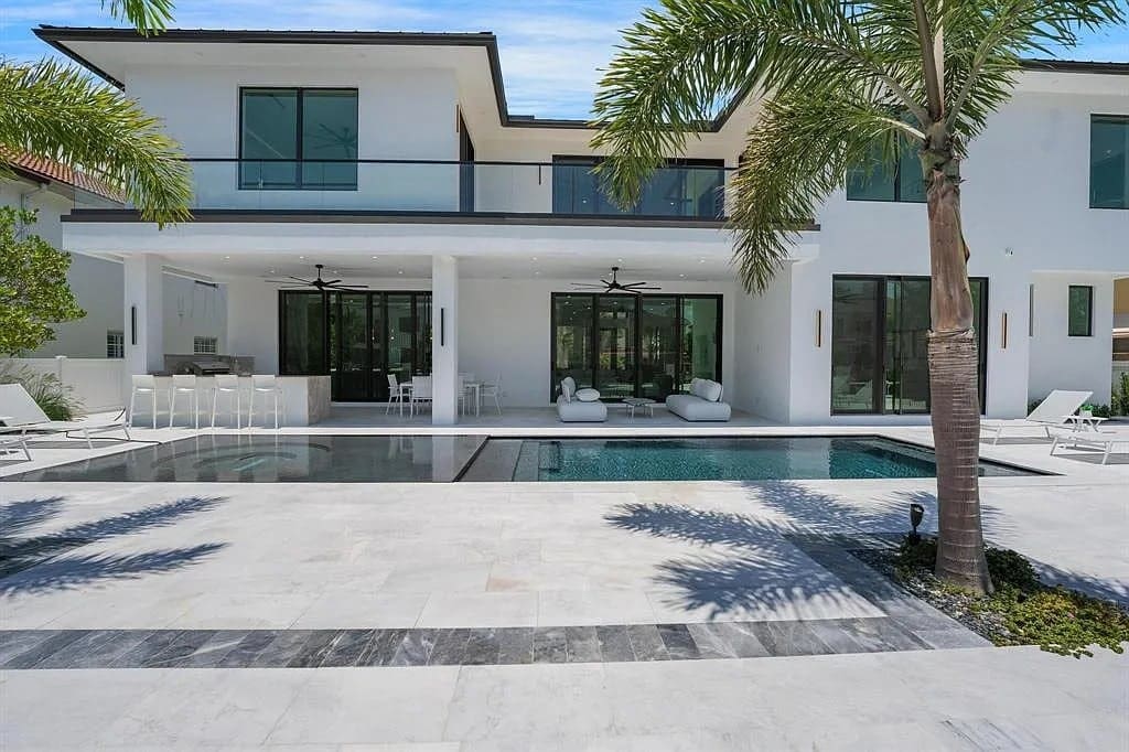 Modern white house with large windows, pool, patio, and palm trees in the foreground.
