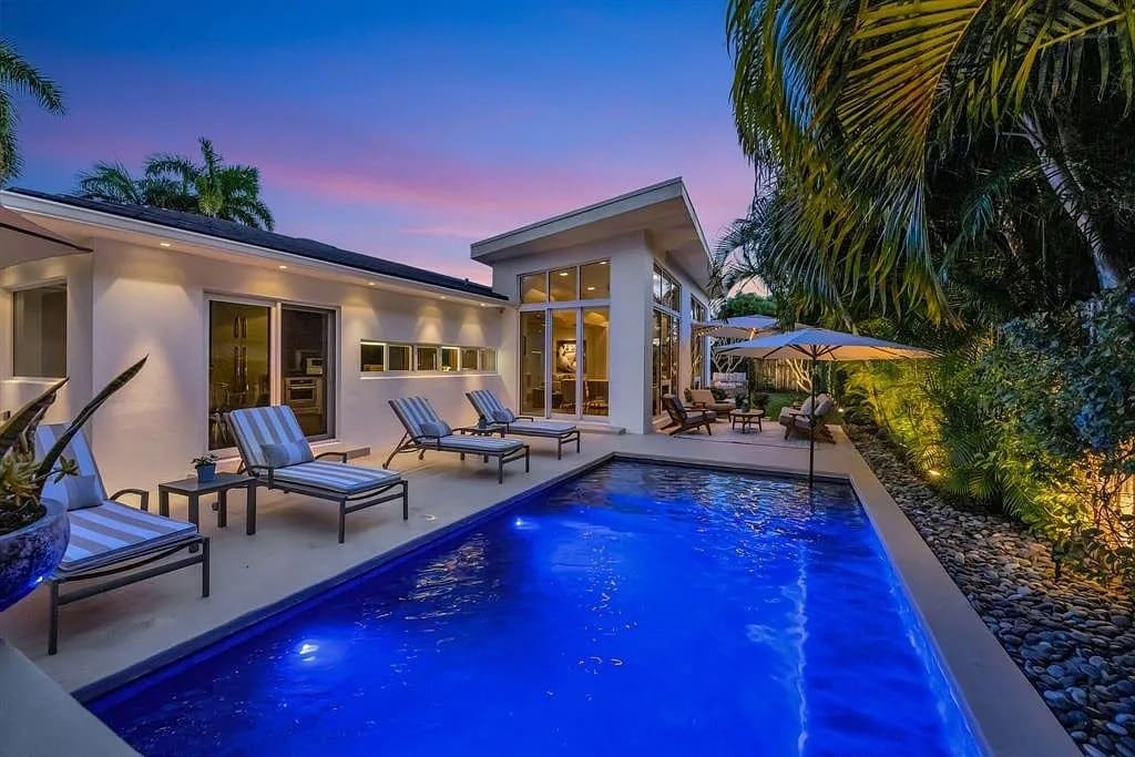 Modern house with large windows, pool, lounge chairs, and tropical landscaping at sunset.
