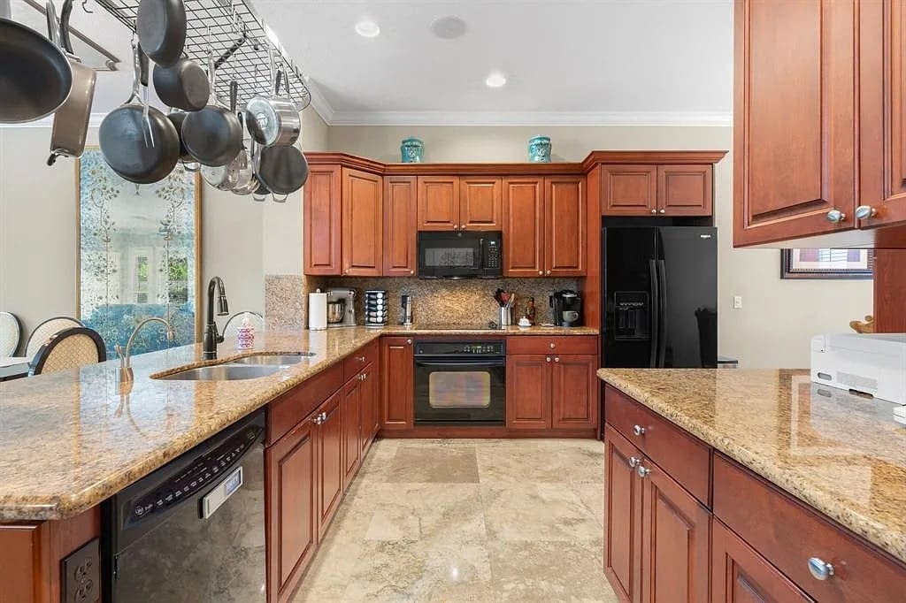 Spacious kitchen with wooden cabinets, granite countertops, hanging pots, and modern appliances.
