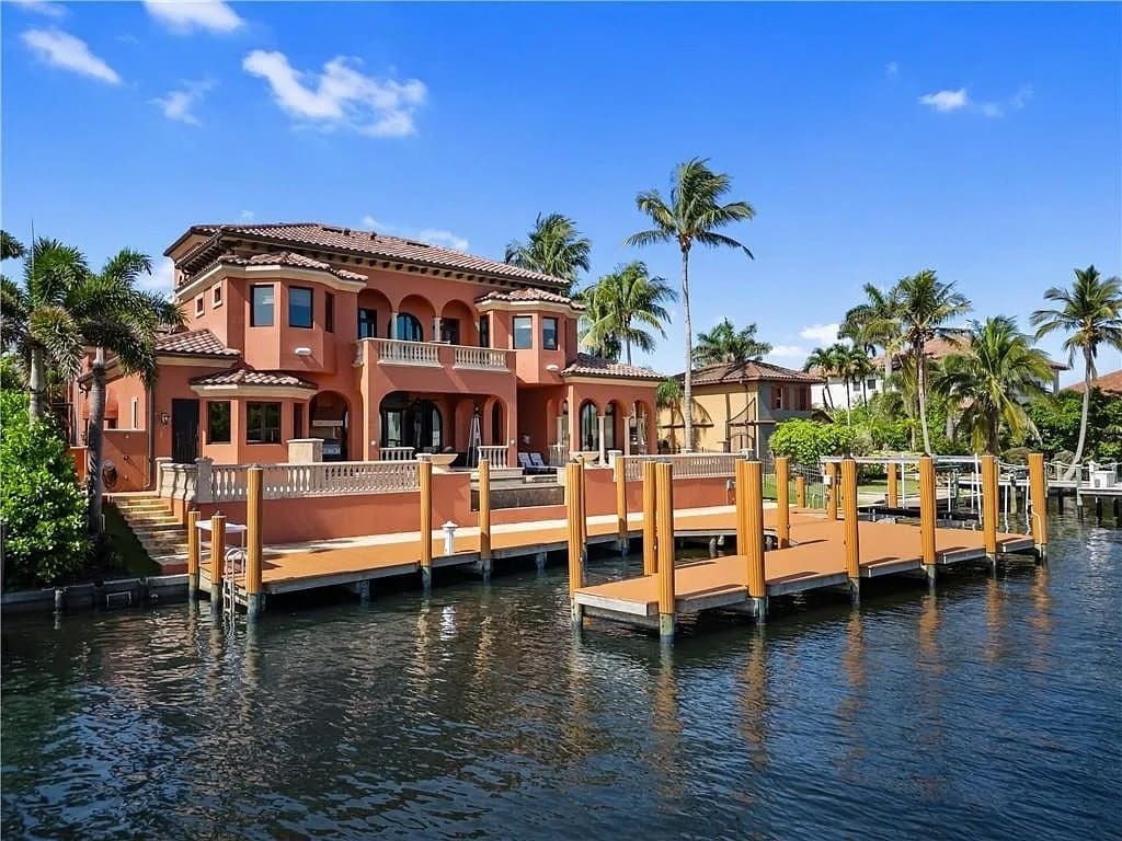 Luxury waterfront house with palm trees, large dock, and clear blue sky.
