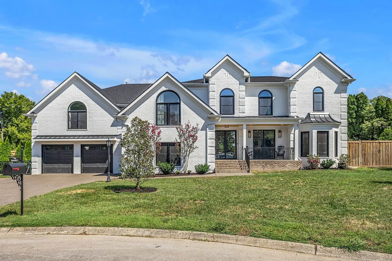 Large white brick house with black garage doors, front porch, and manicured lawn.
