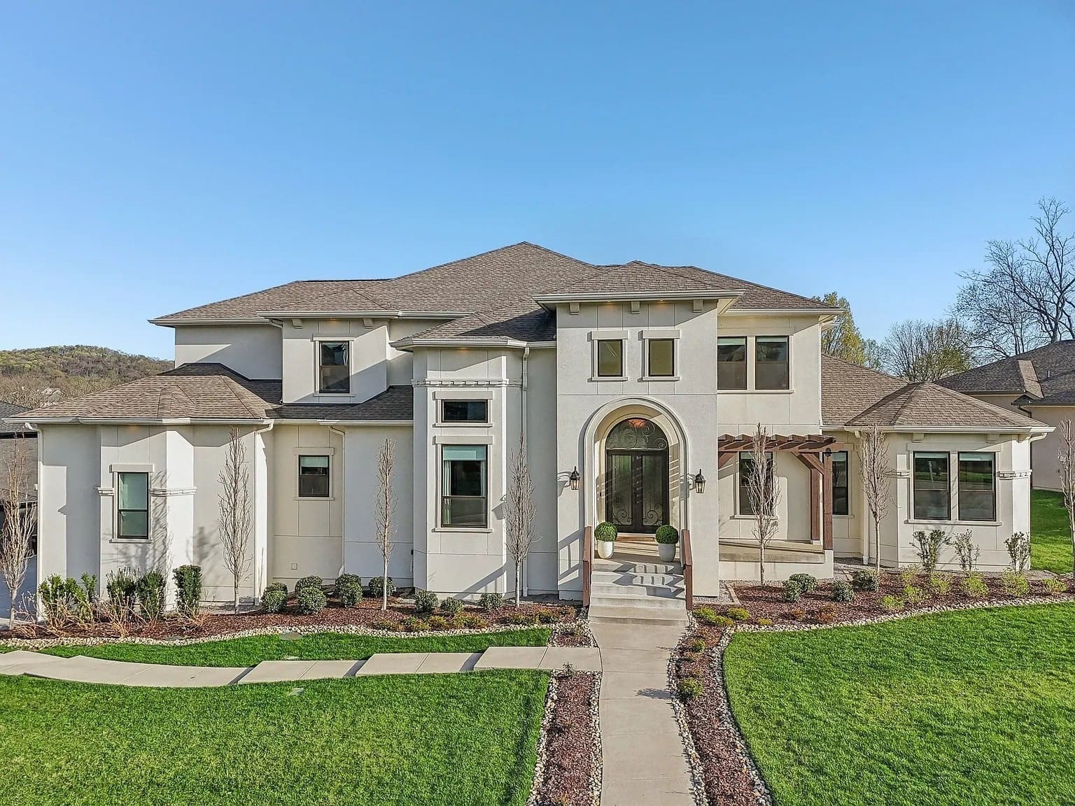 Modern two-story house with large windows, arched entrance, and landscaped front yard.

