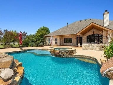 Backyard view of a house with a swimming pool and hot tub under a clear blue sky.
