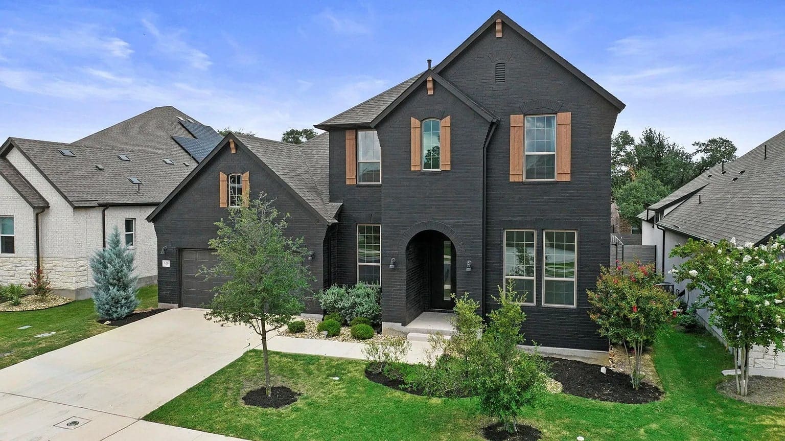 Two-story modern black brick house with arched entryway, surrounded by a green lawn.
