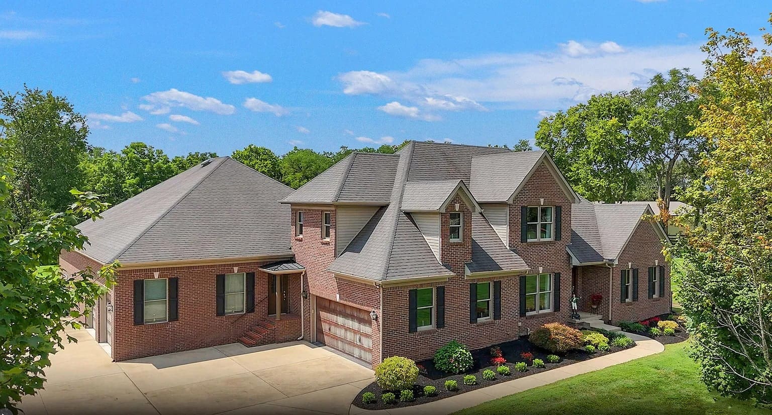 Brick house with gabled roof, driveway, and landscaped yard under a clear blue sky.
