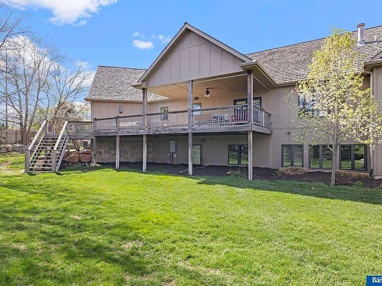 Back view of a large house with a wooden deck overlooking a grassy yard.
