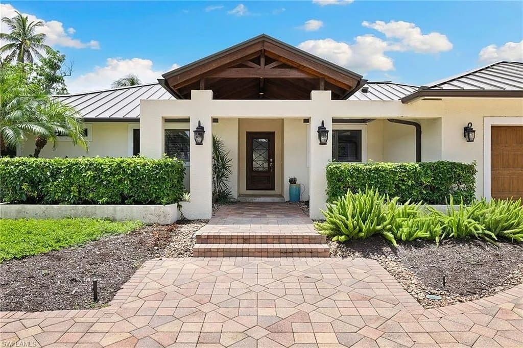 Modern house entrance with a wooden door, white walls, and surrounding greenery.
