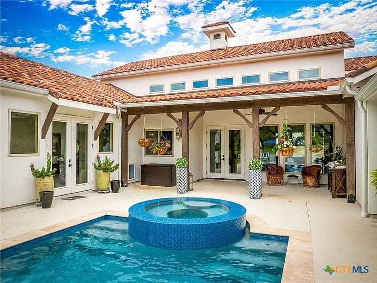 Modern patio with a small round pool, potted plants, and a house with red-tiled roof.
