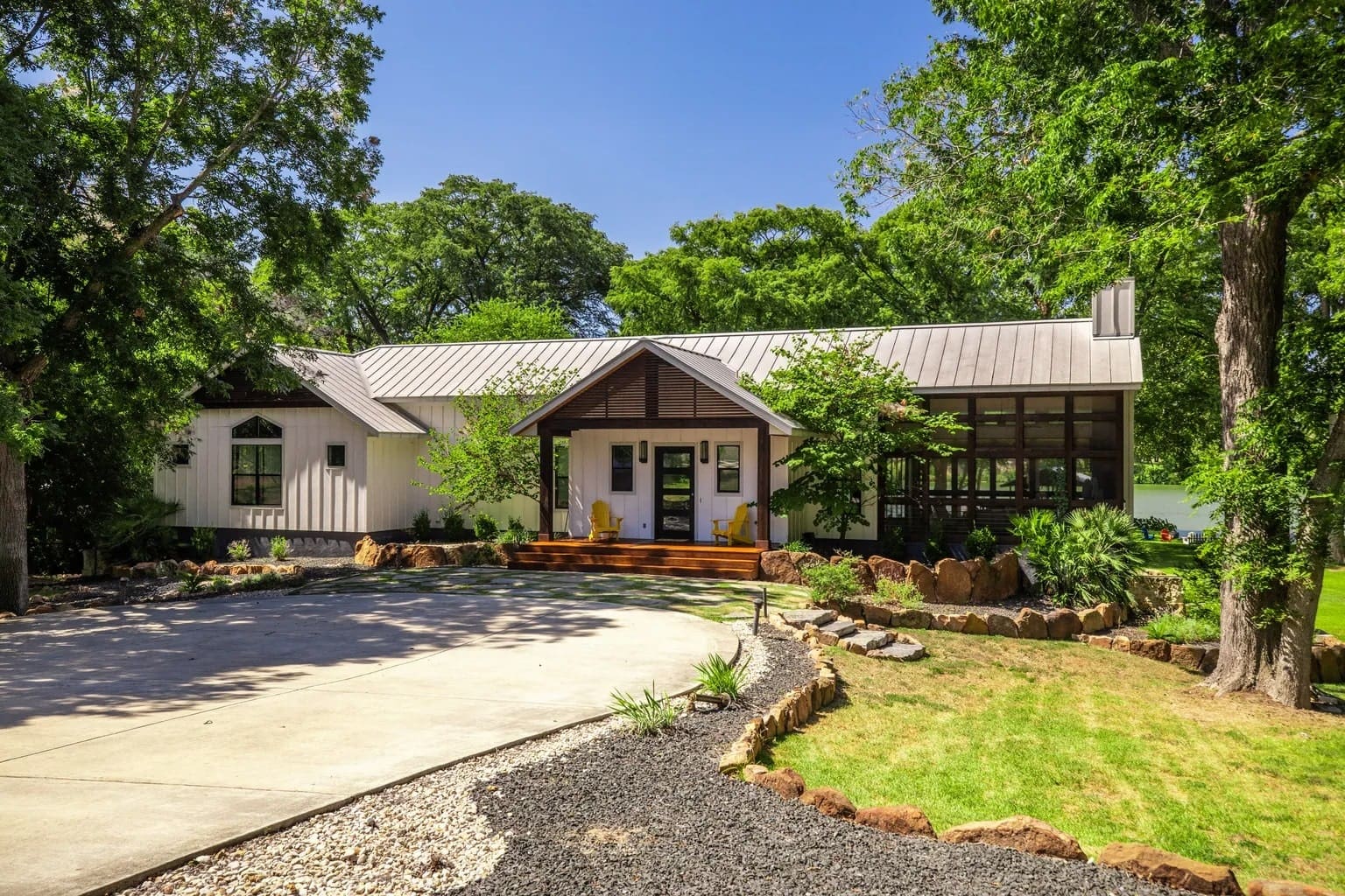 Modern house with a metal roof, surrounded by trees, featuring a landscaped front yard.
