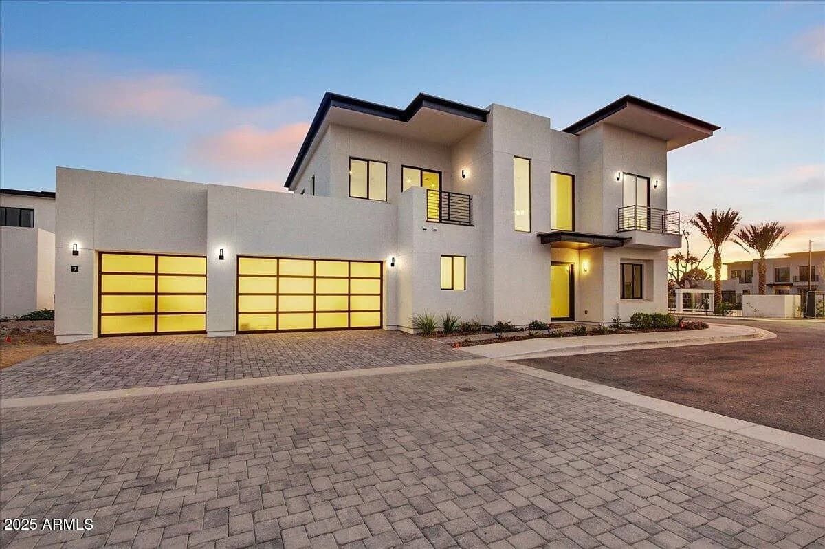 Modern two-story house with large windows, three-car garage, and a paved driveway at sunset.
