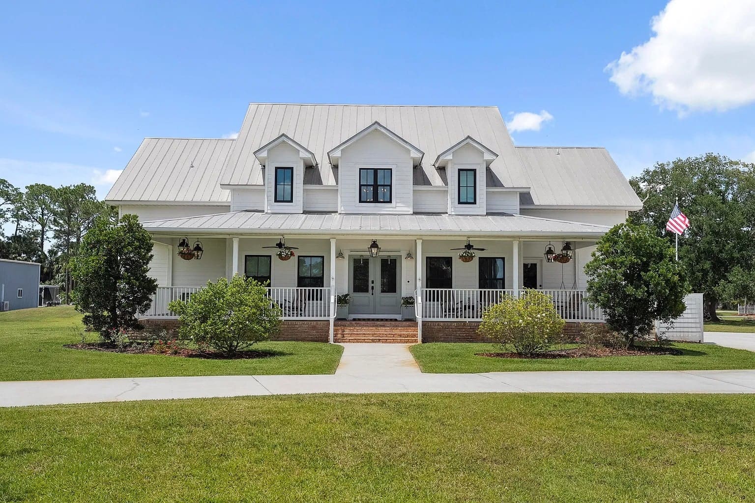 White two-story house with a porch, gabled roof, and American flag on a sunny day.
