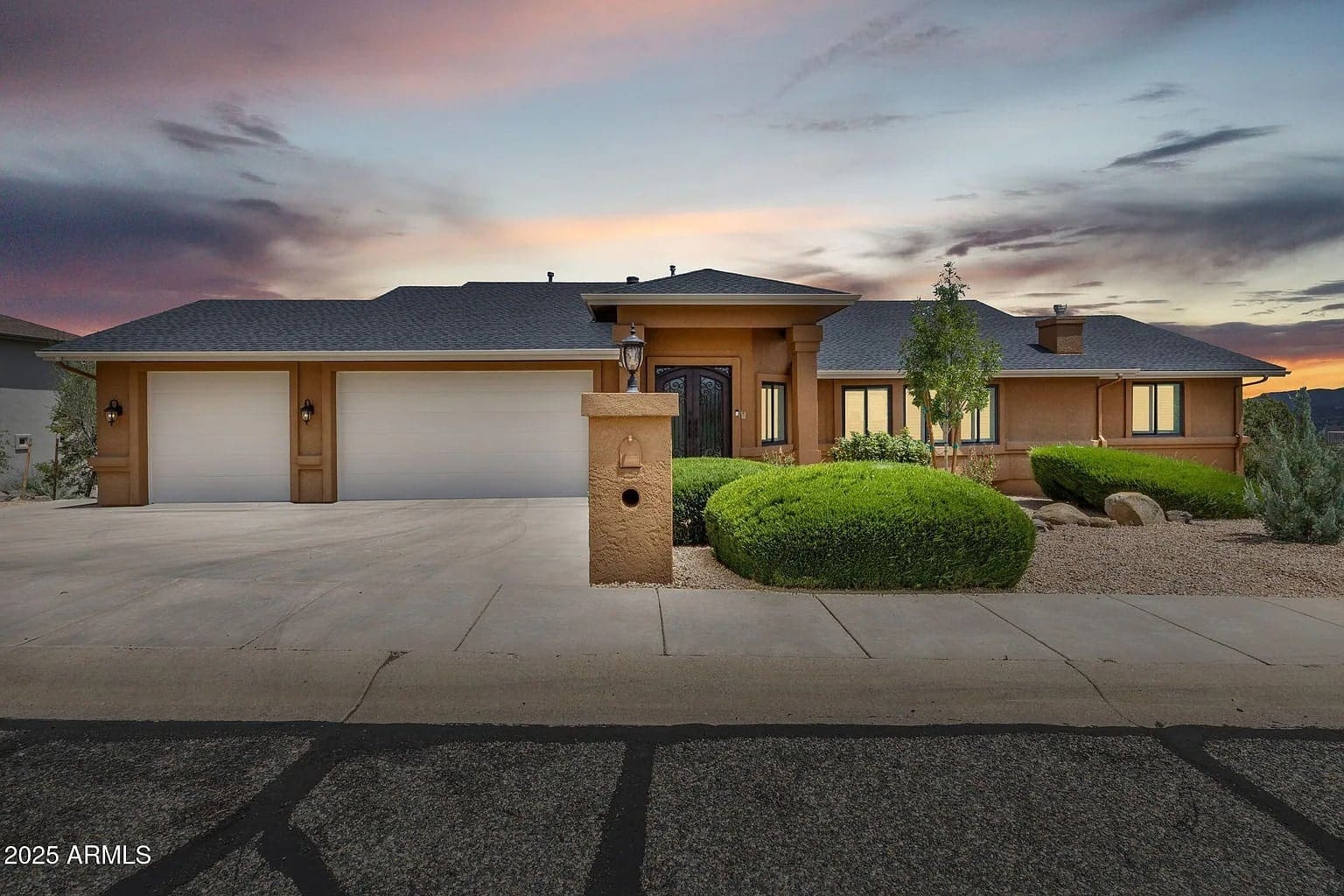 Single-story house with three-car garage, landscaped front yard, and sunset sky backdrop.
