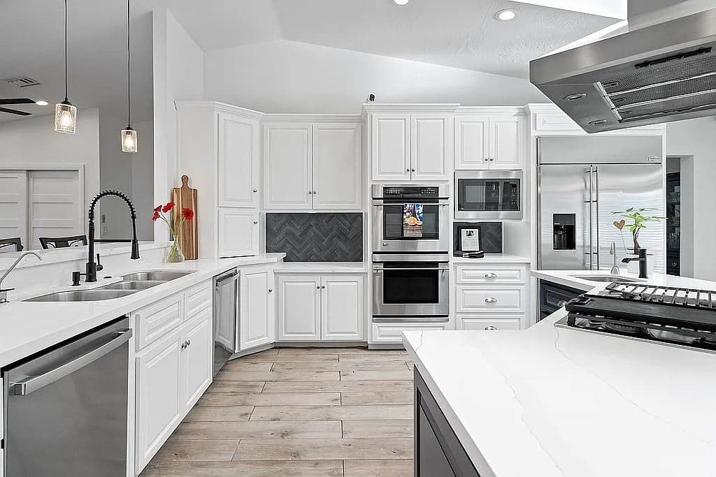 Modern kitchen with white cabinets, stainless steel appliances, and a black herringbone backsplash.
