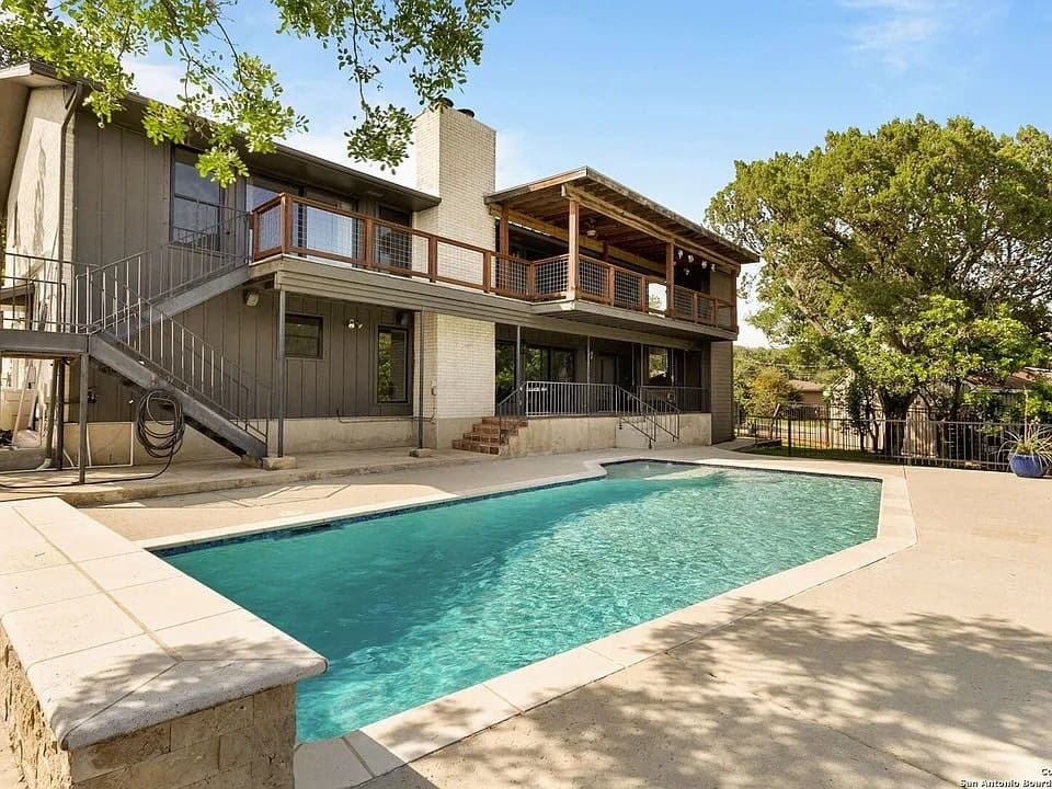 Two-story house with a balcony overlooking a backyard swimming pool and patio area.
