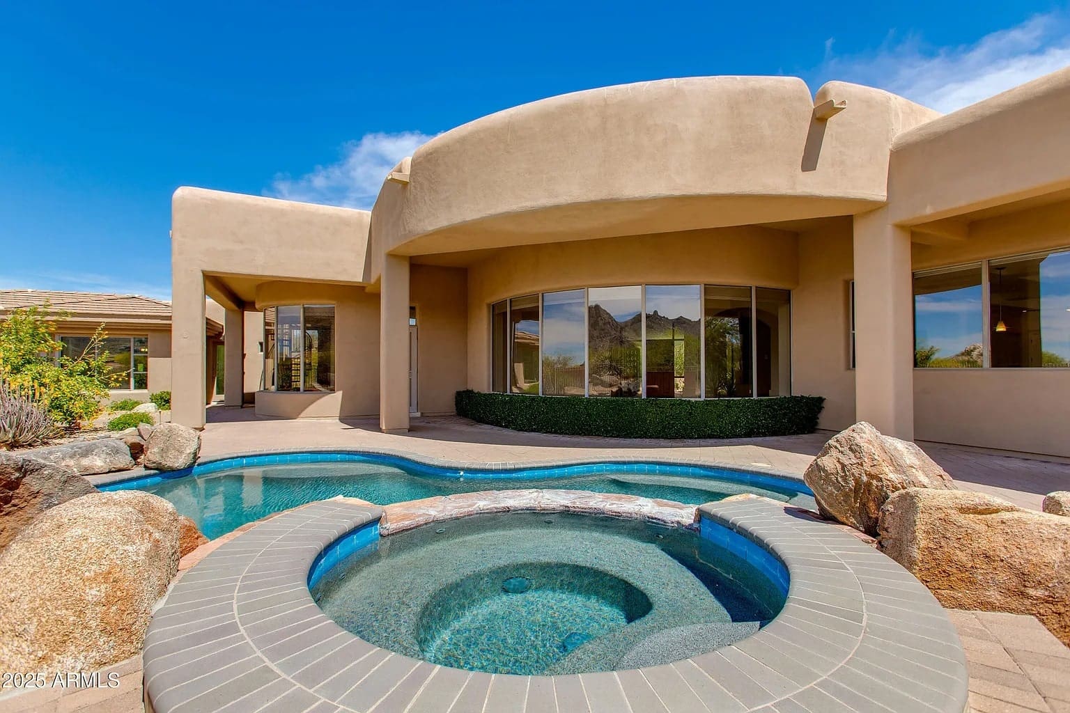 Modern house with curved architecture, large windows, and a small pool in the foreground.
